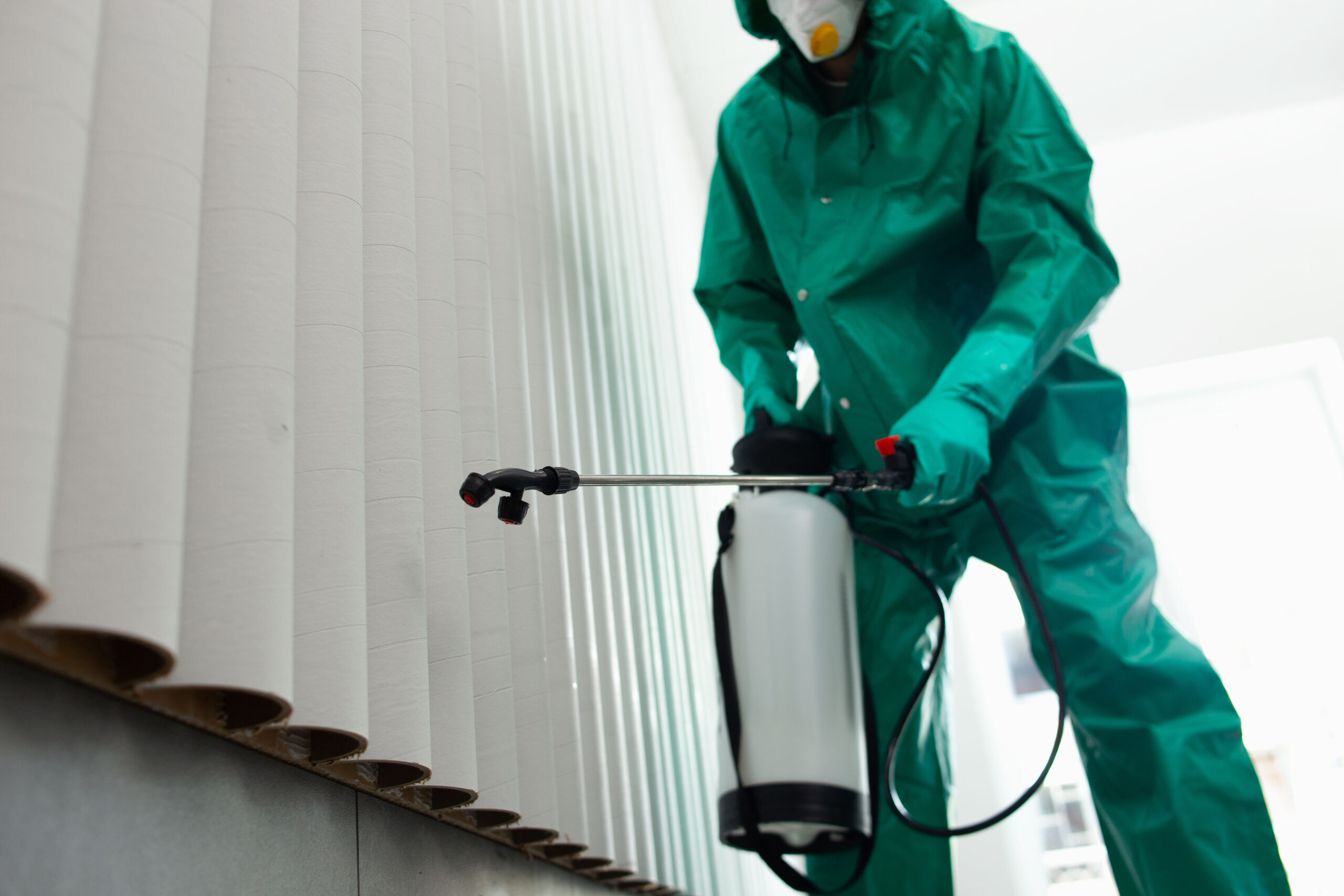 Mann im Ganzkörperanzug schützt sich beim Sprühen von Chemikalien an der Wand