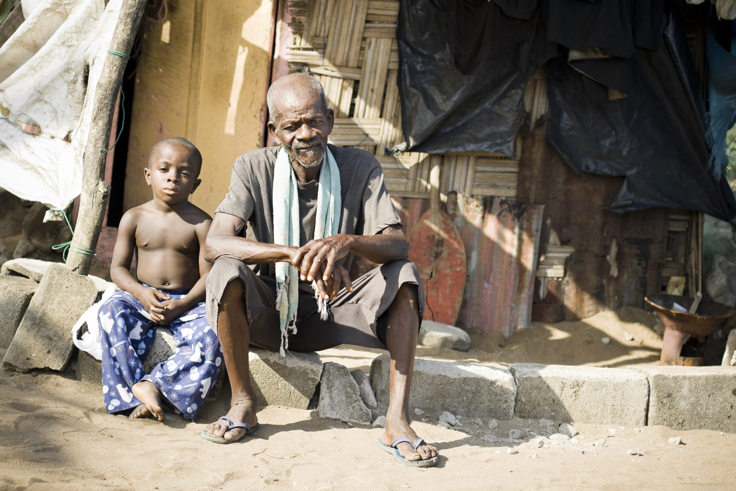 Ein afrikanischer Großvater und sein Enkel sitzen vor einer Hütte