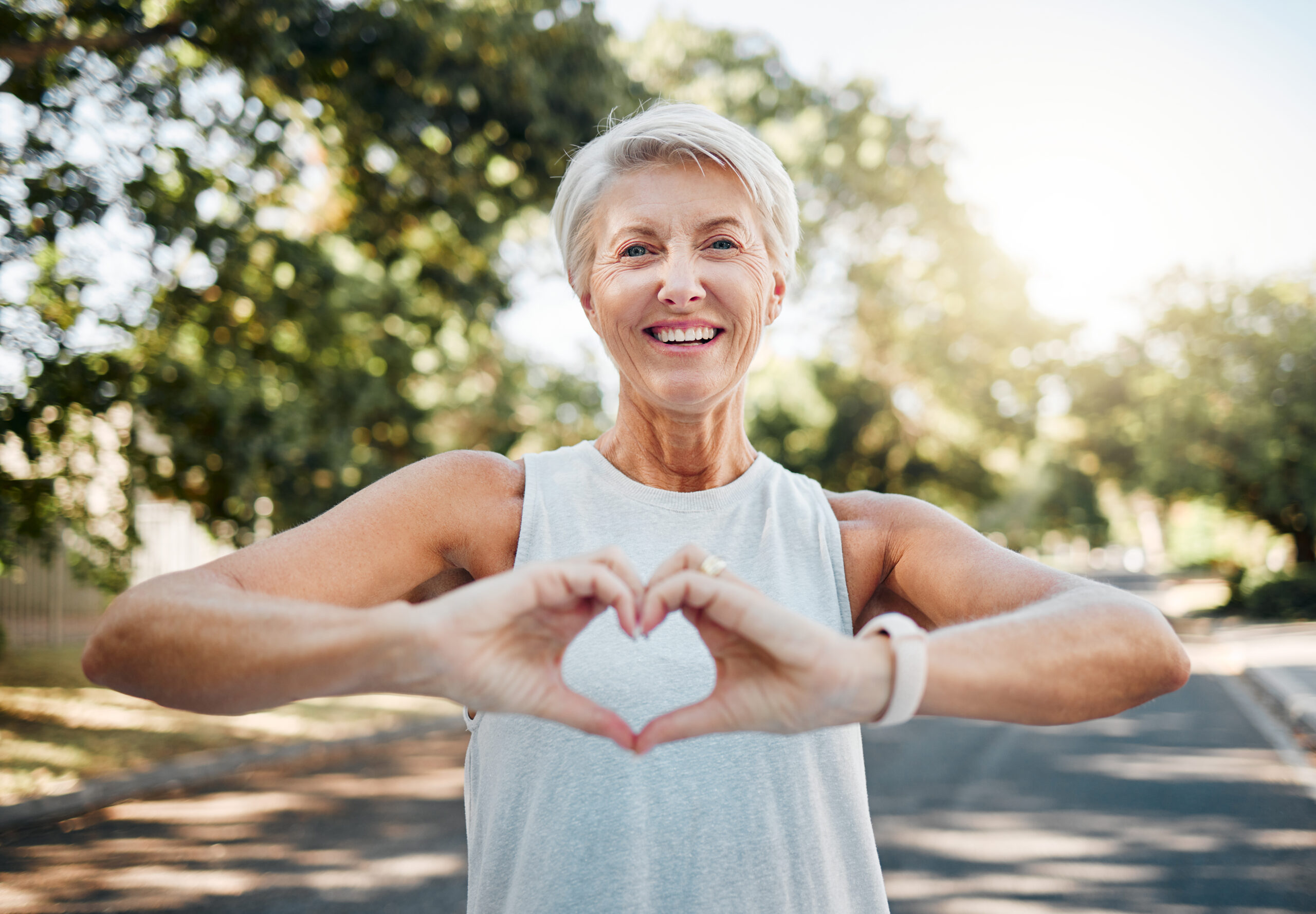 Fitness, glücklich und Herz Hände der alten Frau in der Natur nach dem Laufen für Gesundheit, Wellness und Training. Lächeln, Motivation und Frieden mit älteren Dame und Zeichen für Liebe, Glaube und Ausbildung in der Natur