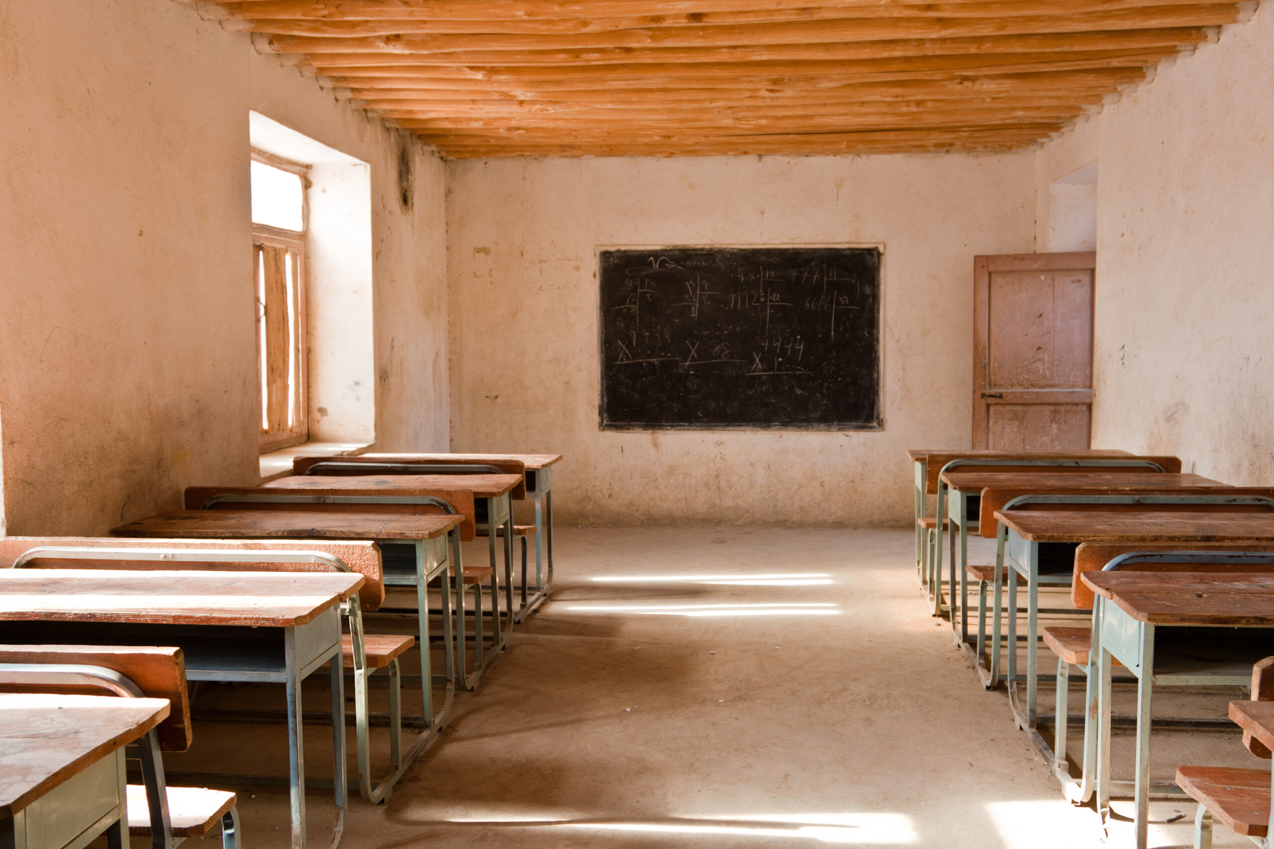 Leeres einfaches Klassenzimmer mit Bänken, Tischen und einer kleinen Tafel