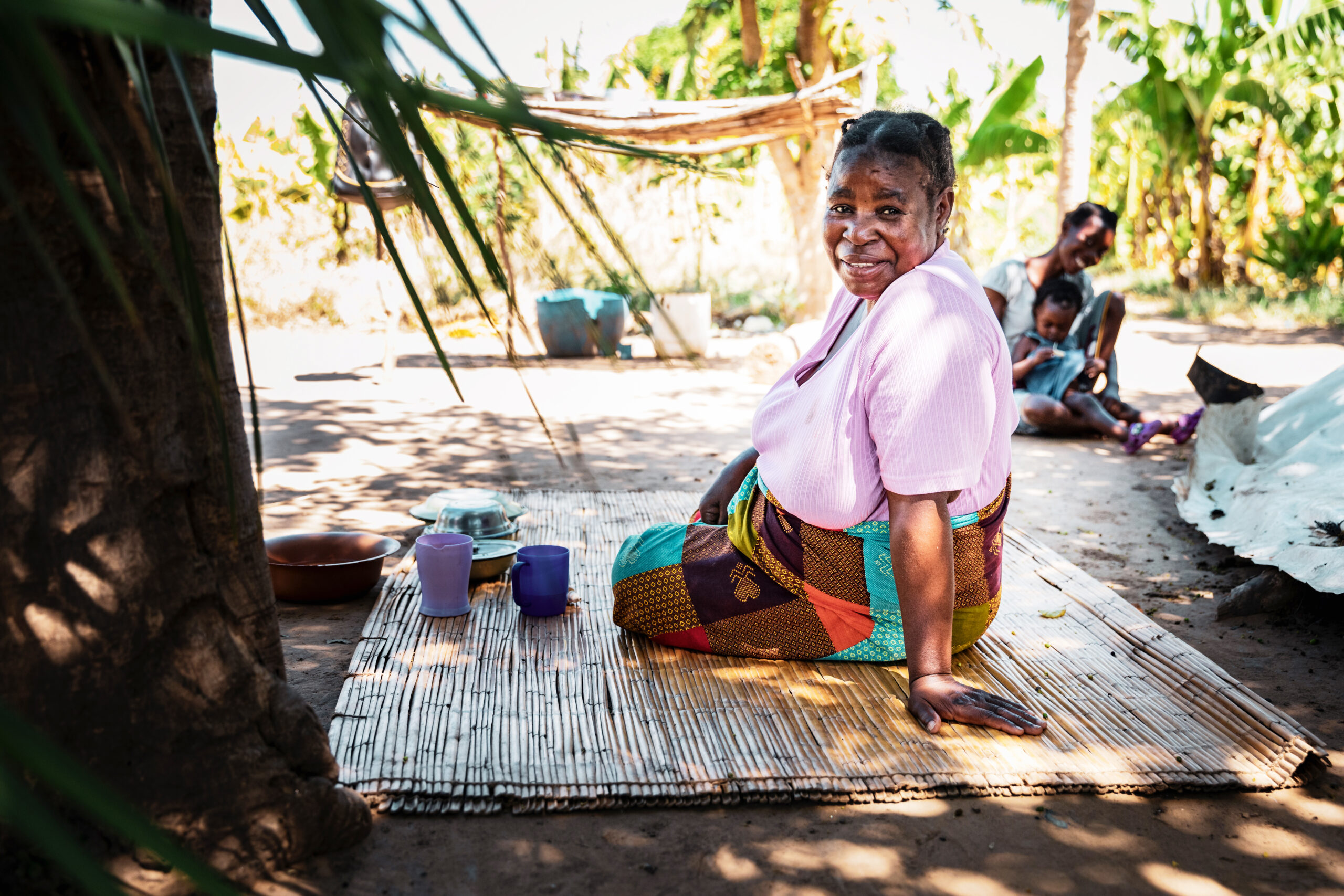 Eine bunt gekleidete afrikanische Frau sitzt auf einem Teppich und lächelt in die Kamera