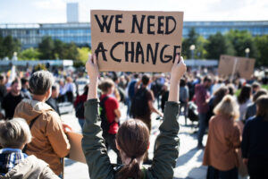 Person hält selbst gestaltetes Poster hoch, auf dem steht We need a change