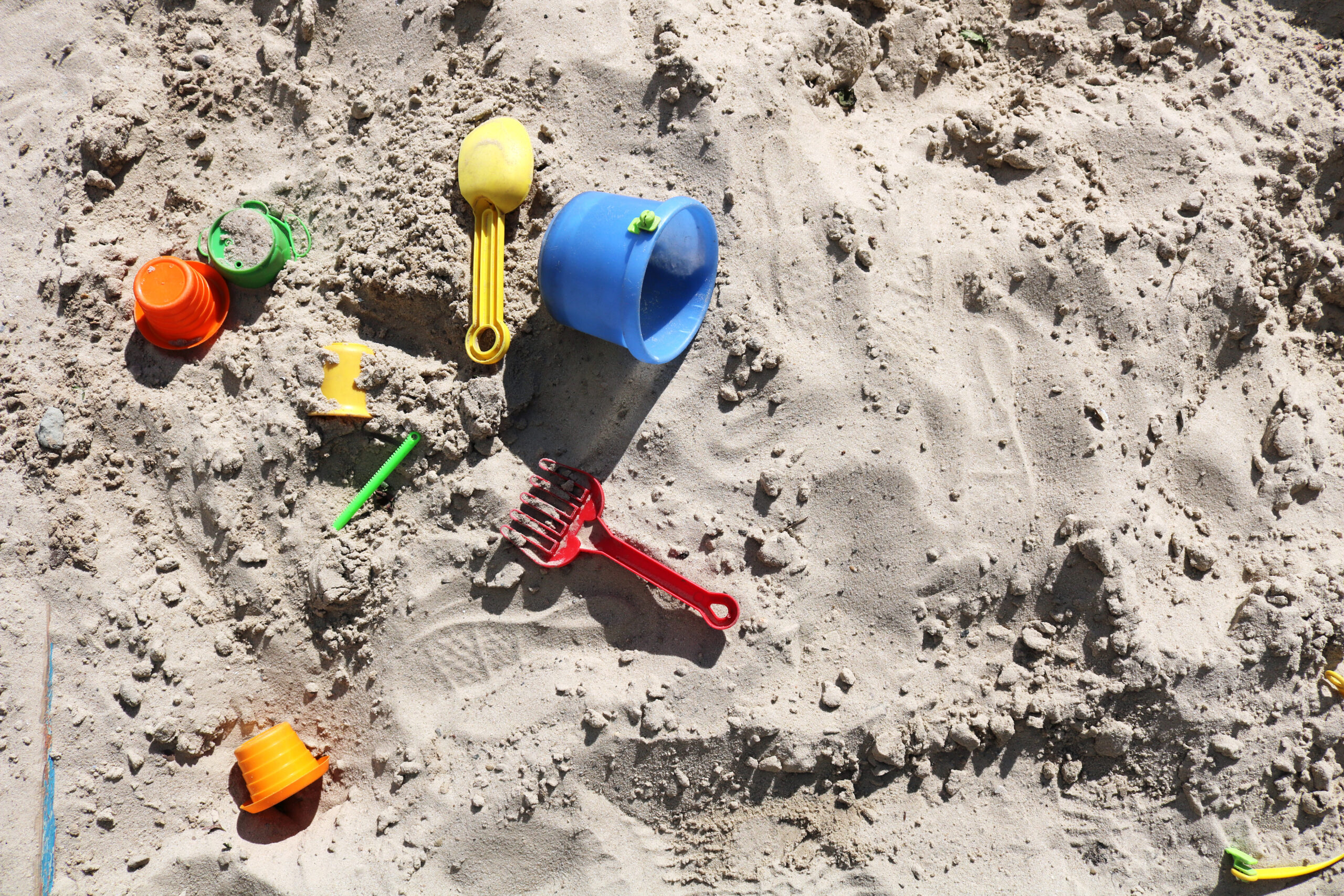Buntes Kinderspielzeug liegt im Sandkasten.