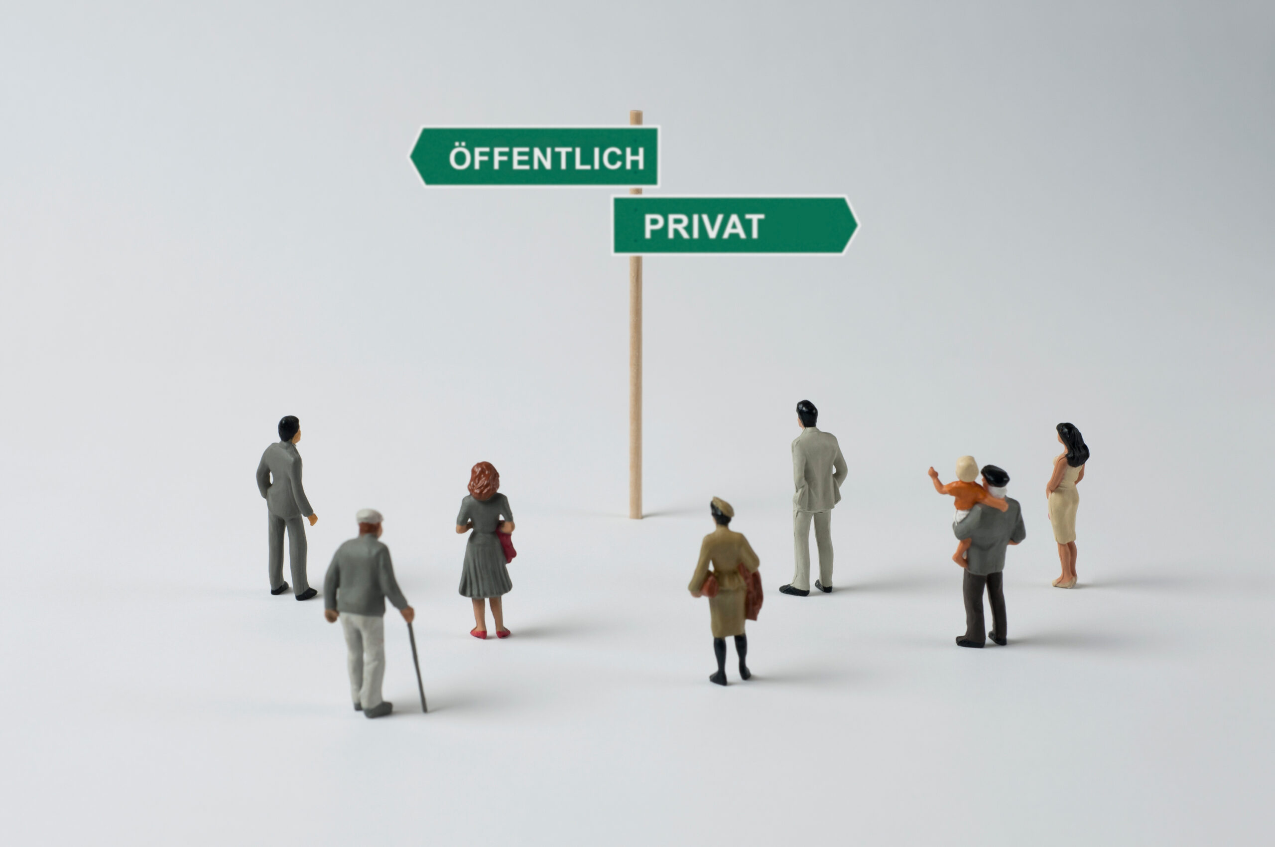 Miniaturfiguren stehen vor einem Wegweiser mit den Richtungen „Öffentlich“ und „Privat“.